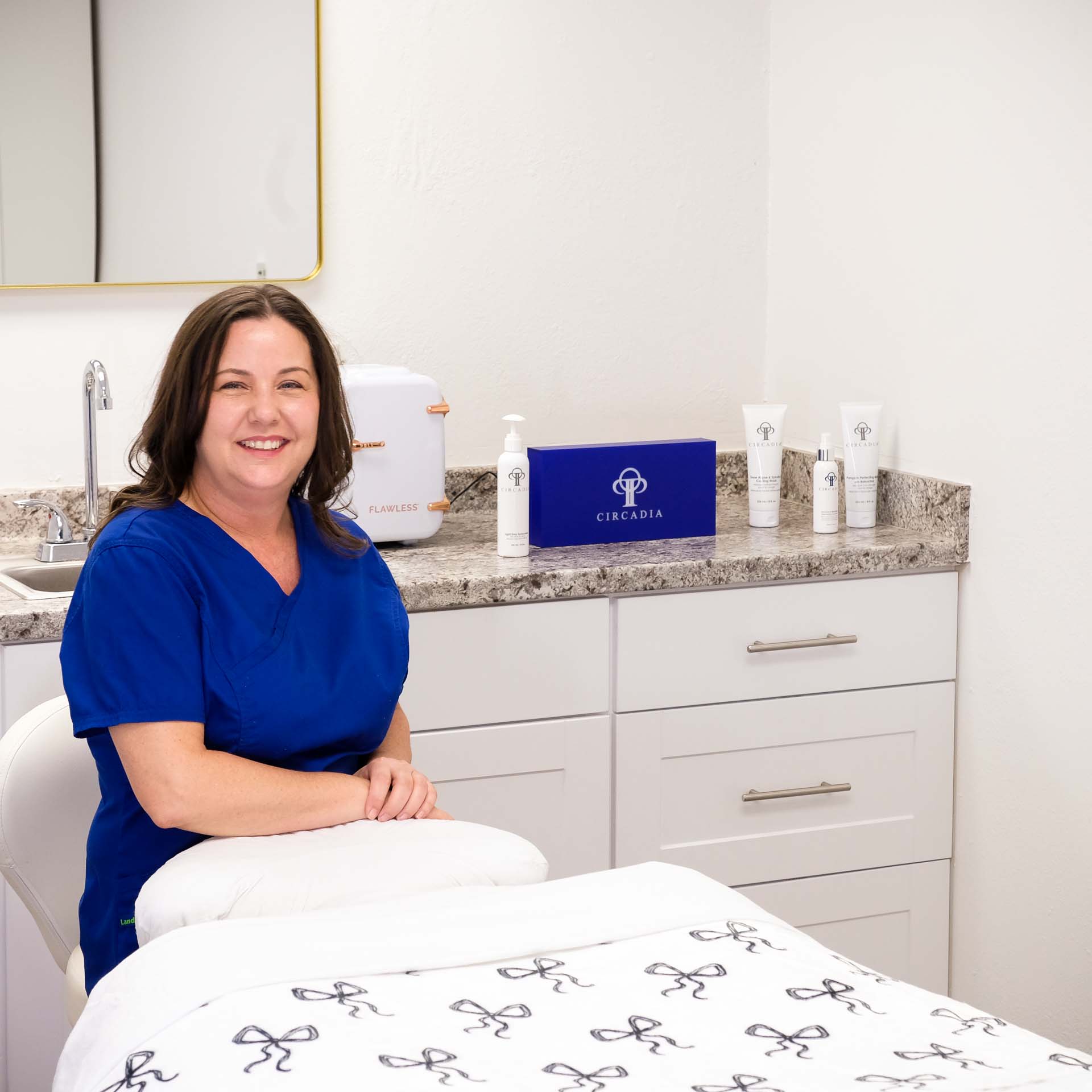 Sonya Dilbeck, an esthetician, is seated on a stool
							behind her treatment table. Behind her is a counter that displays some of her treatment
							products and a blue Circadia promotional plaque.